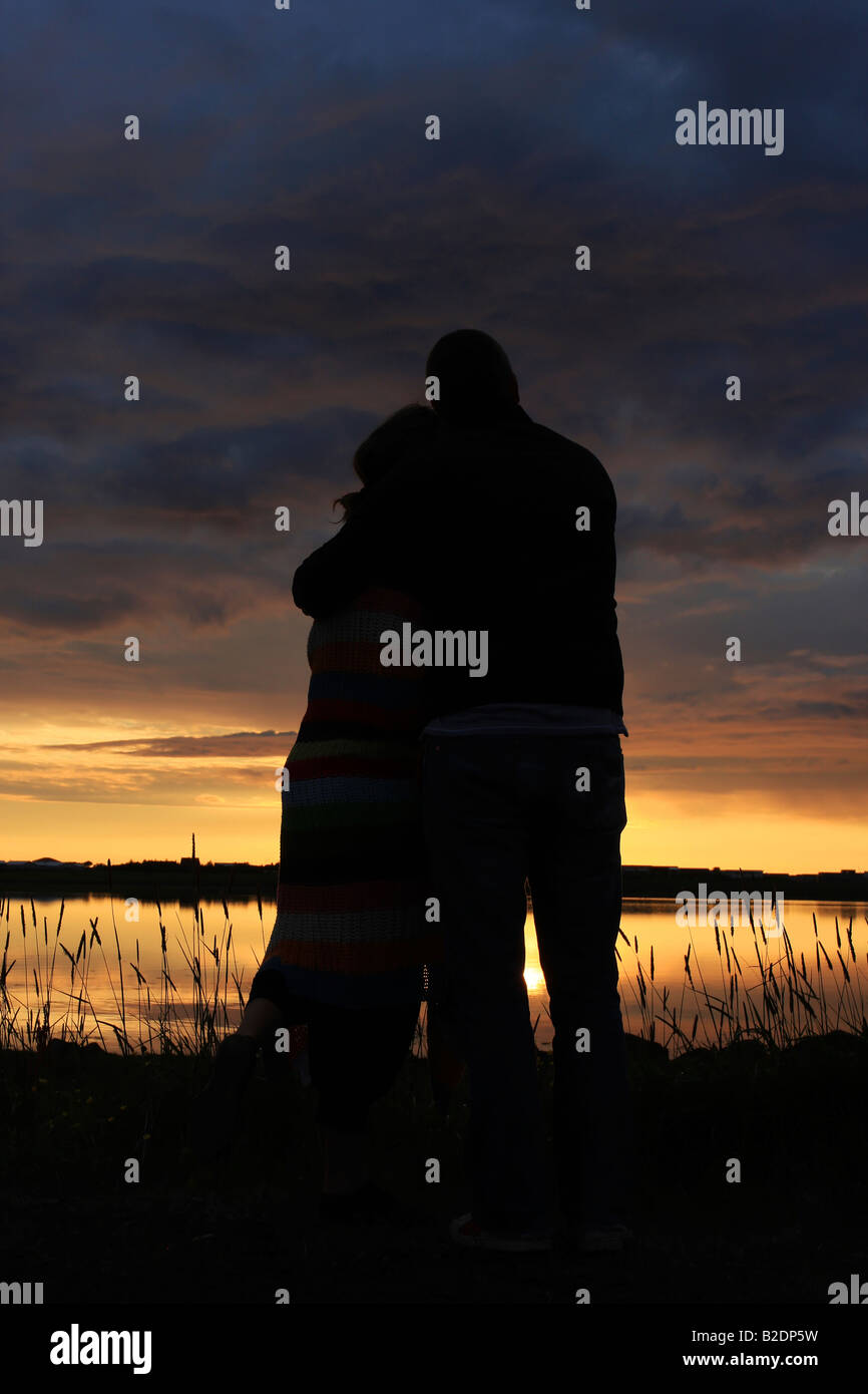 Glückliches junges Paar einander halten und beobachten den Sonnenuntergang Silhouette von ihnen gesetzt gegen die untergehende Sonne Stockfoto