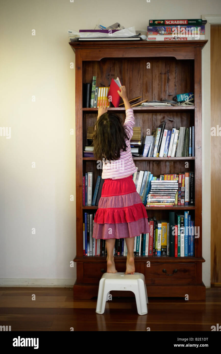 Fünf Jahre altes Mädchen verwendet Schritte, Buch im Bücherregal zu erreichen Stockfoto