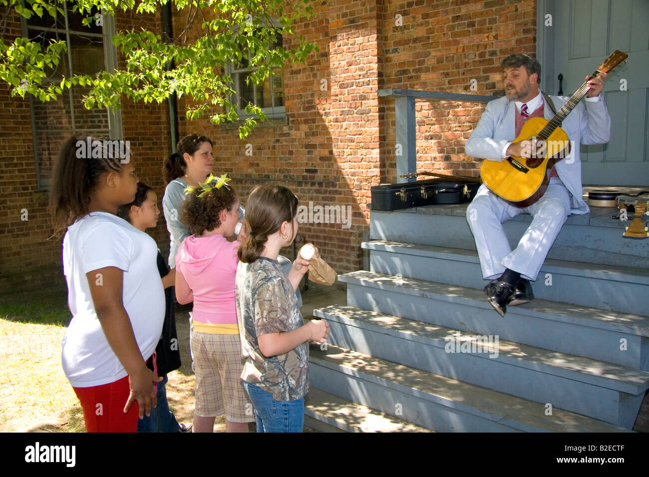 Kinder sehen einen Musiker das Gitarrespielen in Greenfield Village in The Henry Ford in Dearborn, Michigan Stockfoto
