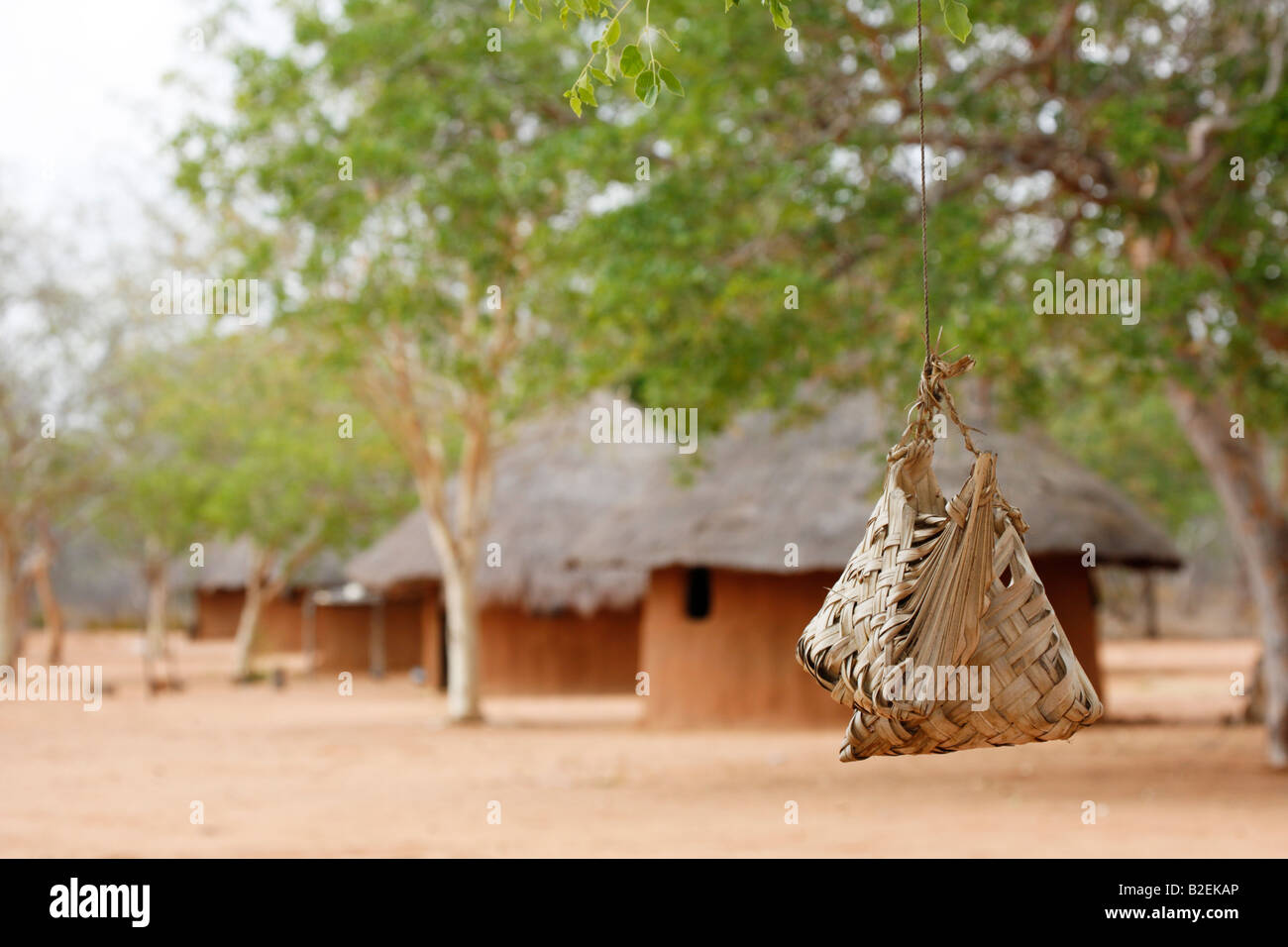 Handgewebte Palmblatt Taschen hängen unter einem Baum in einem lokalen Dorf vor dem Hintergrund einer Reihe von Hütten in einem afrikanischen Dorf Stockfoto