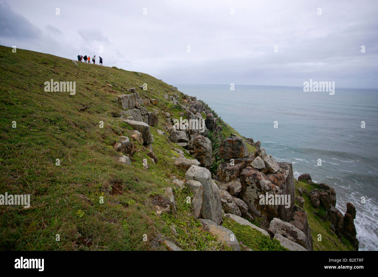 Eine Gruppe von Touristen auf einem grasbewachsenen Hang mit Blick auf die Bucht Morgan Klippen und das Meer Stockfoto