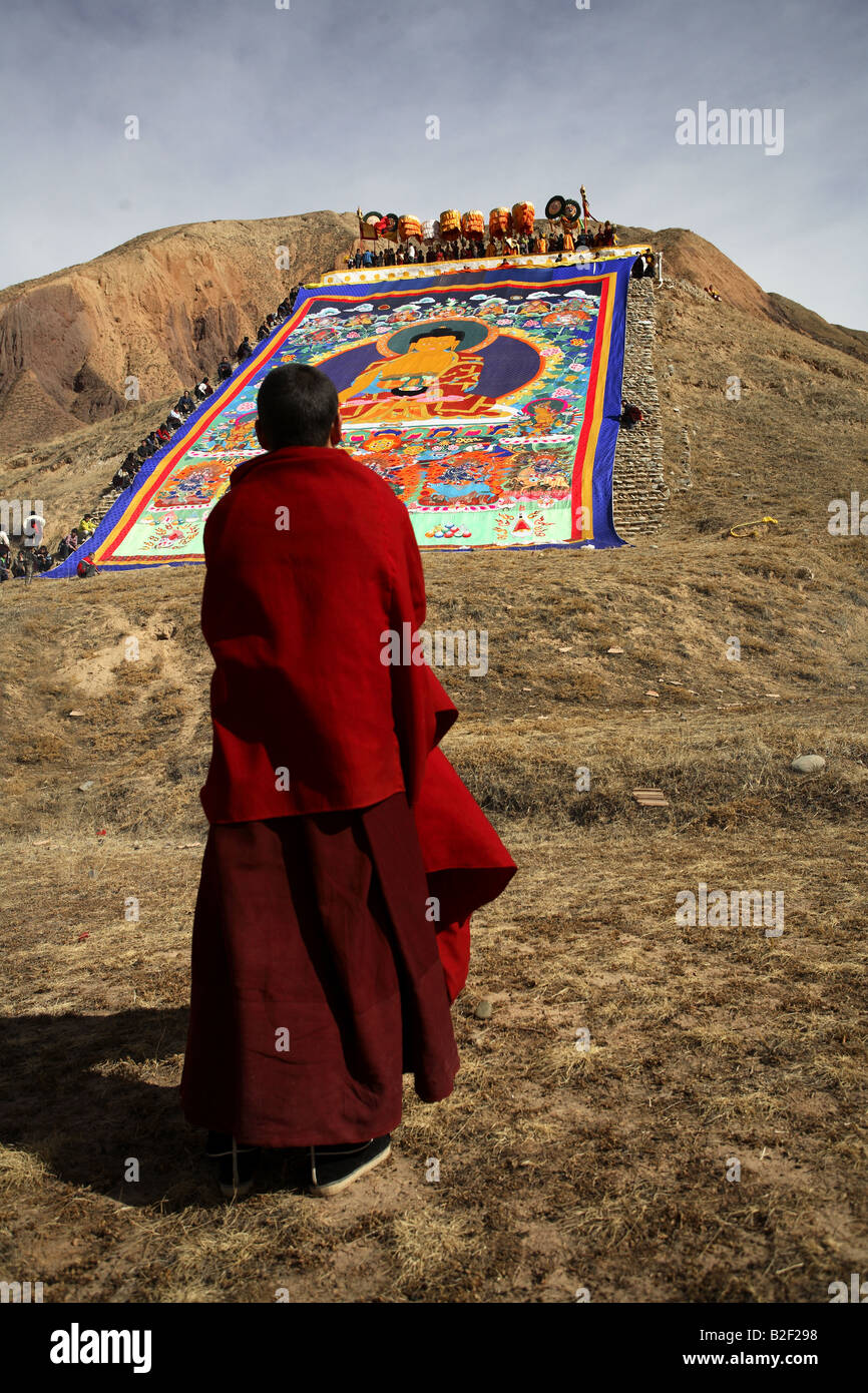 Ein buddhistischer Mönch betet vor eine riesige Thangka Stockfoto