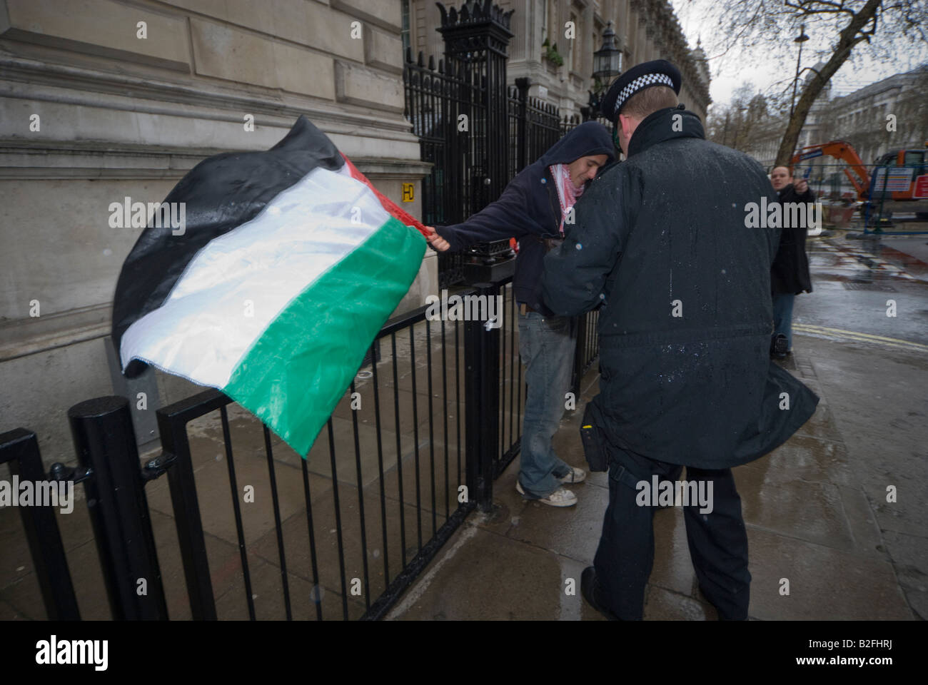 Polizist nähert sich jungen Mann mit palästinensischen Fahne am Geländer neben Downing St aus Protest gegen die israelische Blockade des Gaza-Streifens Stockfoto