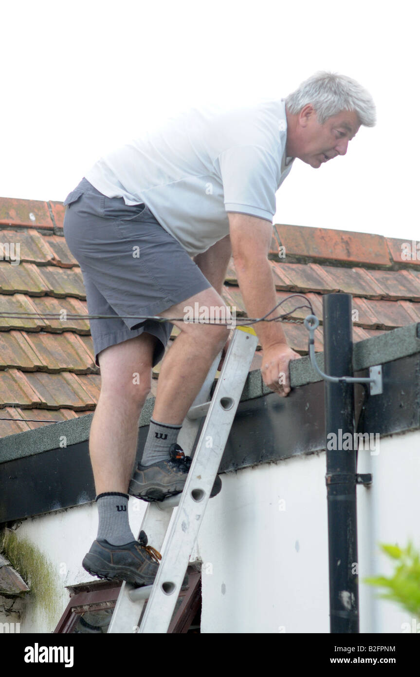 Ein Mann steigt eine Leiter vom Dach eines Hauses in Cornwall, Großbritannien Stockfoto