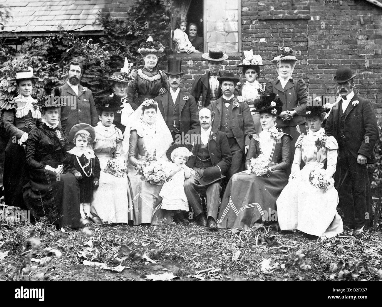 1899 Foto, viktorianische Hochzeitsgruppe. Im Freien mit Bridge and Groom in der Mitte, im Halbkreis sitzend, alles in viktorianischer Kleidung. Blickkontakt. Stockfoto