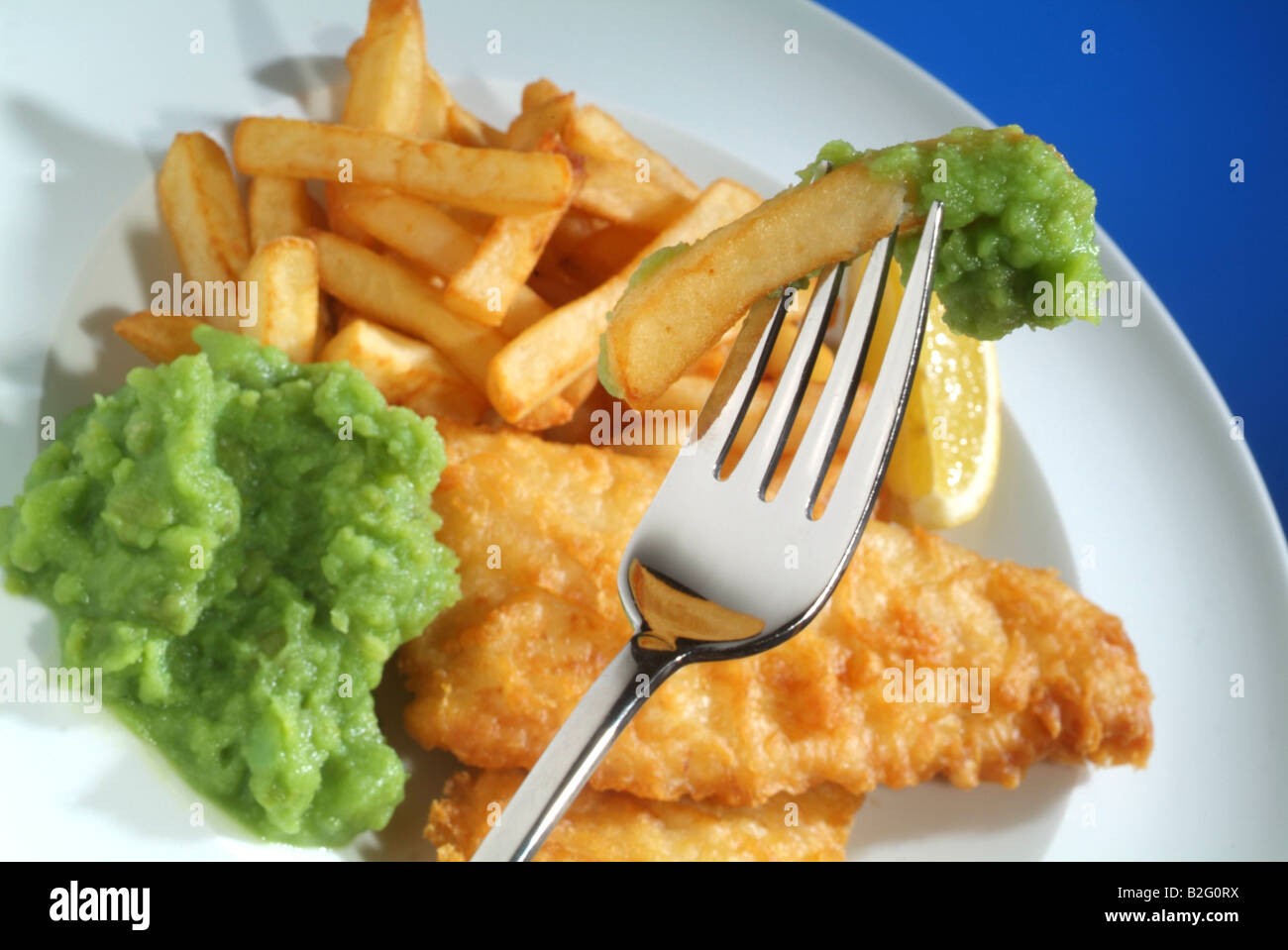 Fisch, Chips und Erbsenpüree auf einem weißen Teller mit einer Gabel geschlagen Stockfoto