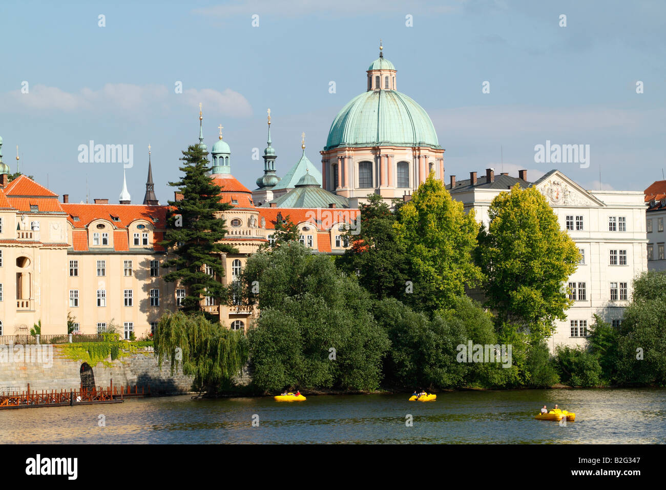 Die Türme und die Kuppel des Clementinum, die über die Moldau mit Bäumen und roten Dach Gebäude im Vordergrund aus gesehen Stockfoto