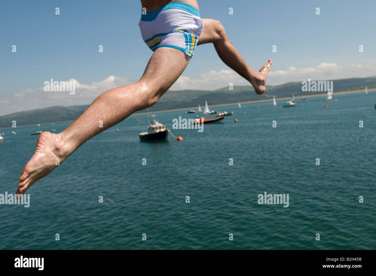 Nahaufnahme von den Beinen eines Mannes springen auf den Steg oder Pier in Aberdyfi in den Dyfi Fluss Mündung Sommernachmittag Wales UK Stockfoto
