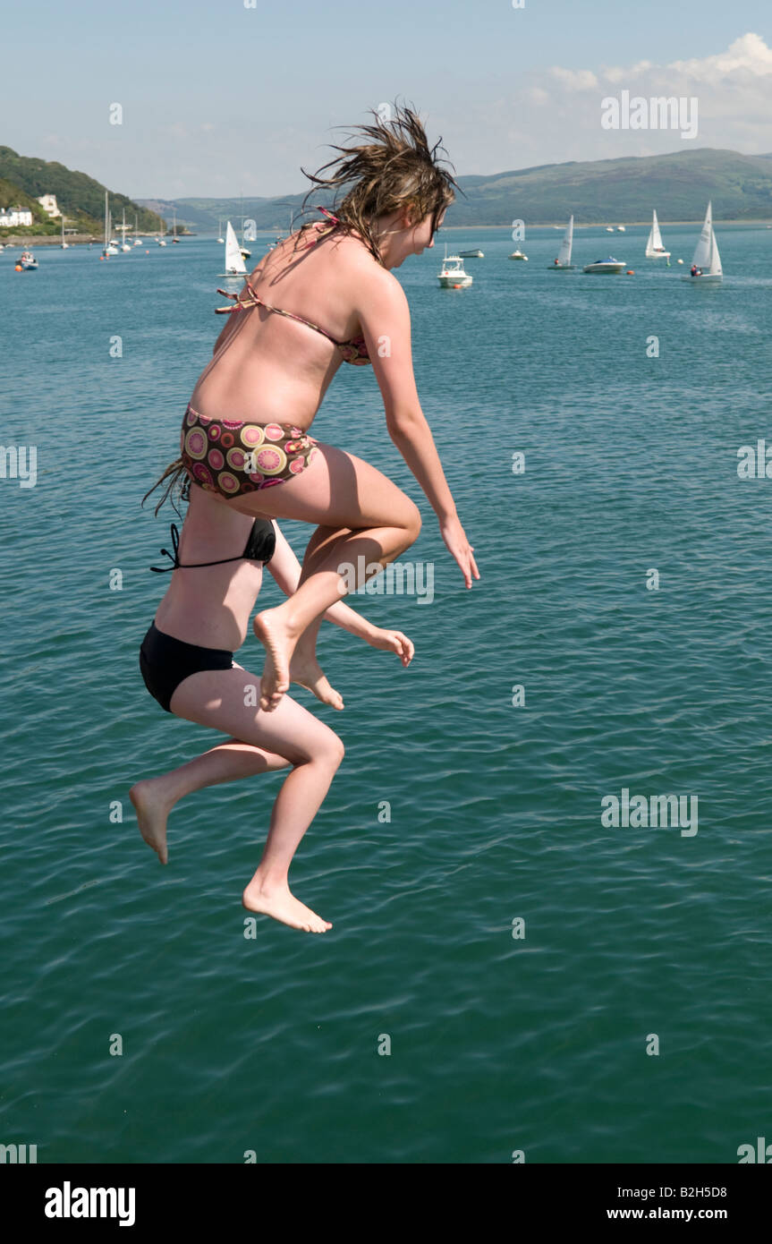 Zwei Mädchen im Teenageralter springen auf der Mole in Aberdyfi in den Dyfi Fluss Mündung Sommernachmittag, Wales UK Stockfoto