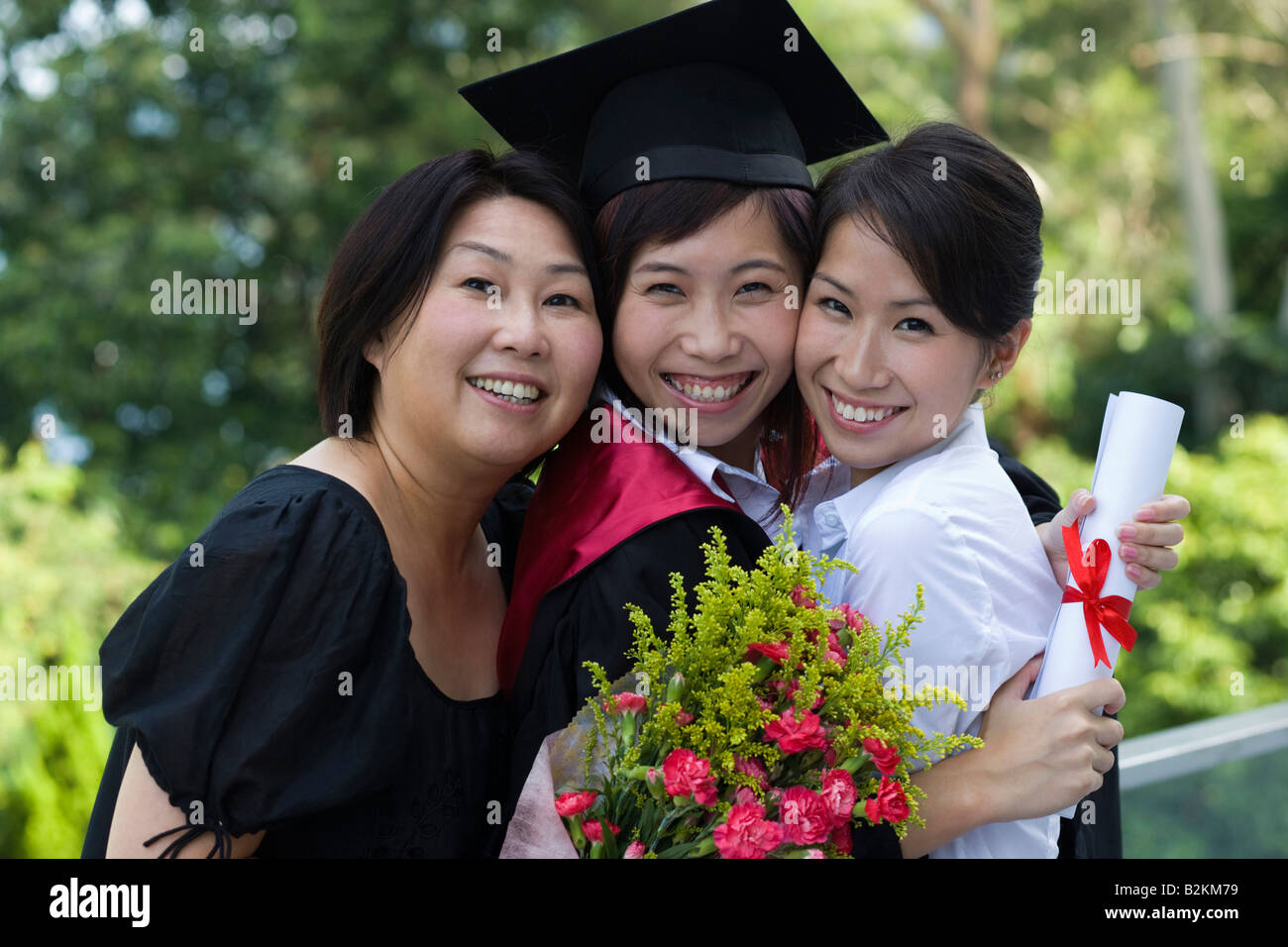 Porträt von Mitte Erwachsene weibliche Absolventin Diplom und umarmen ihre Schwestern Stockfoto