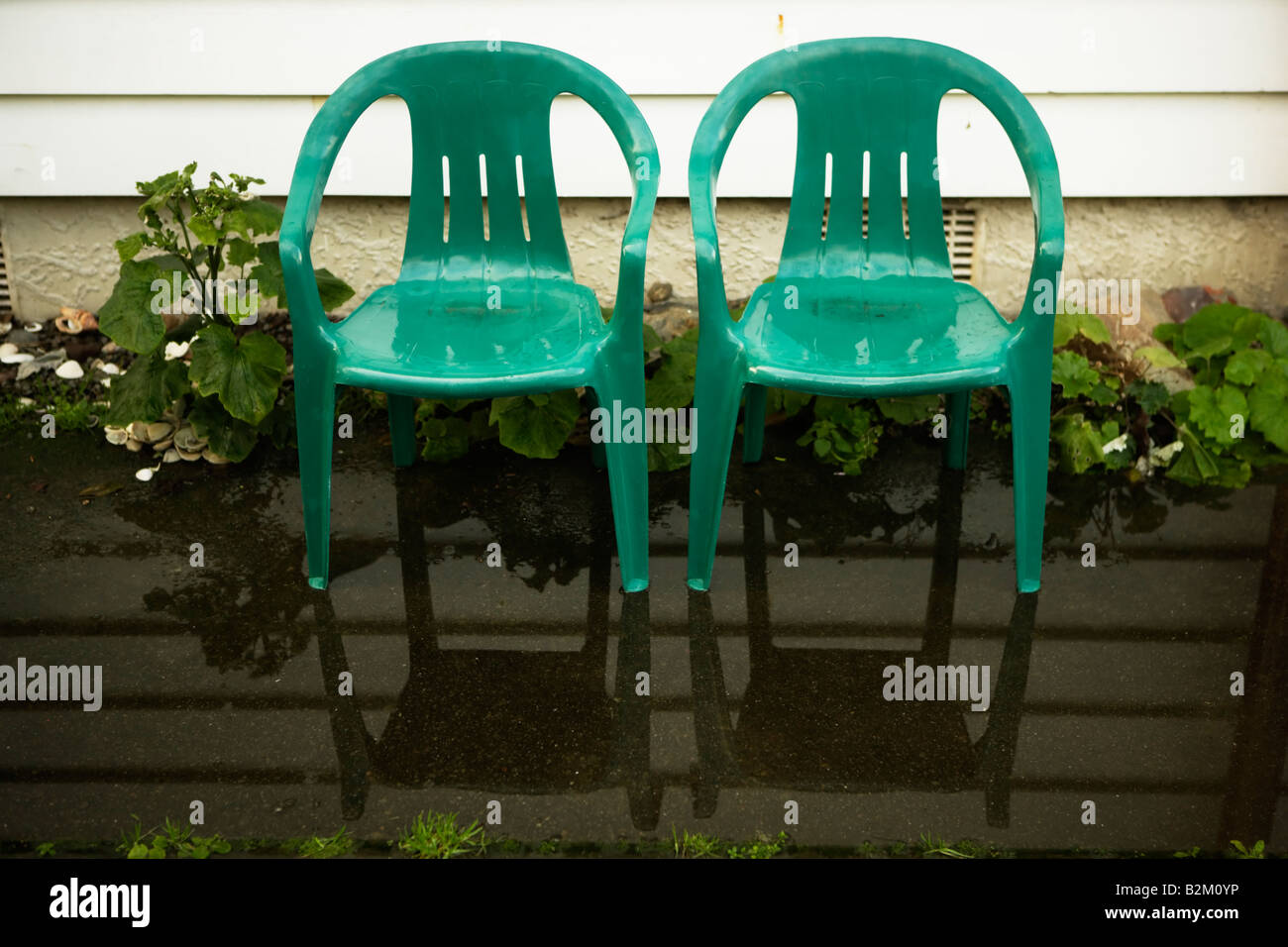 Zwei kleine Kinder s Kunststoff Gartenstühle stehen in einer Pfütze neben einem Wetterschenkel Haus Stockfoto