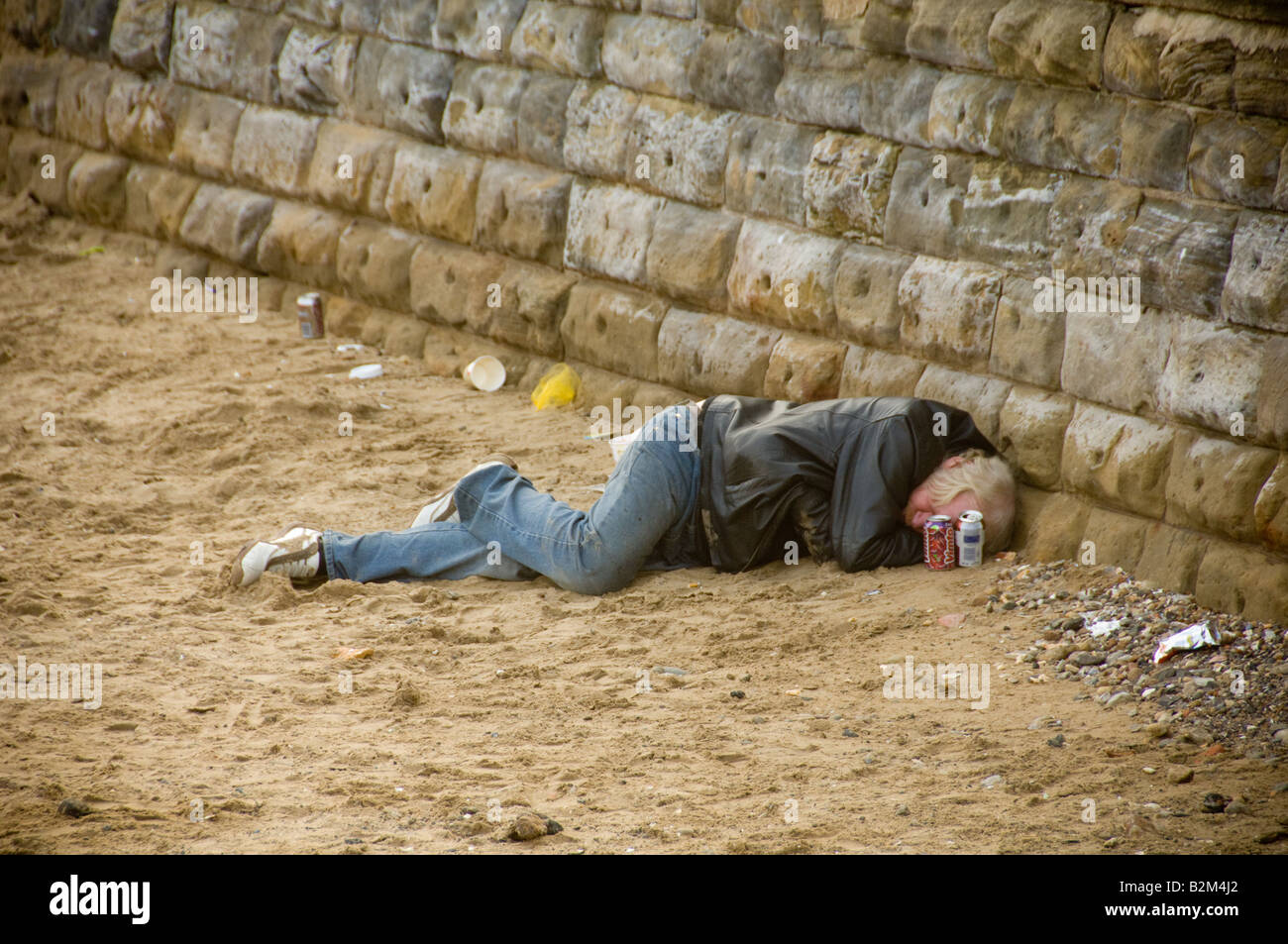 Ein erwachsener weißer Mann, der lässig gekleidet ist und Jeans und eine Lederjacke trägt, schläft am Strand von Scarborough. North Yorkshire. UK. Stockfoto