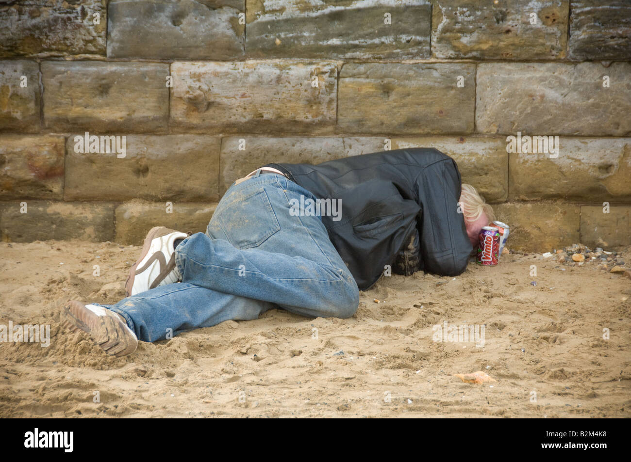 Ein nicht identifizierbarer, reifer, weißer Mann, der lässig gekleidet ist und Jeans und eine Lederjacke trägt, schläft am Strand von Scarborough. North Yorkshire. UK. Stockfoto