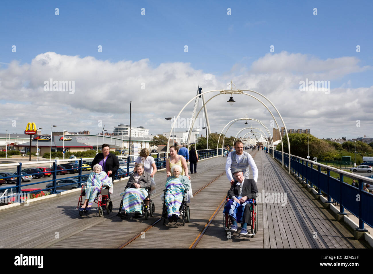 Vier Menschen, ältere behinderte Männer und Frauen Rentner im Rollstuhl entlang Pier. Southport, Merseyside England Großbritannien Stockfoto