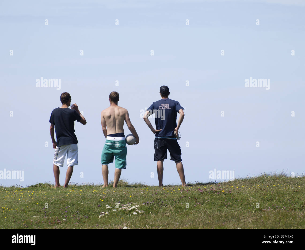 Drei junge Männer stehen auf einem Hügel mit Blick auf Meer Stockfoto