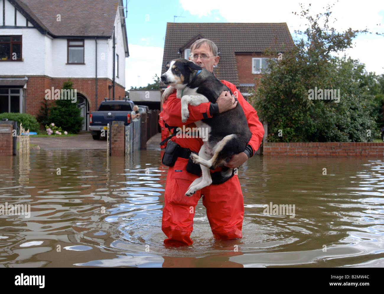 EINE RSPCA FLUT RETTUNG OFFIZIER TRÄGT EIN HUND IN EINER ÜBERFLUTETEN STRAßE WO HÄUSER SIND DURCH HOCHWASSER ABGESCHNITTEN WORDEN IN TEWKESBUR Stockfoto