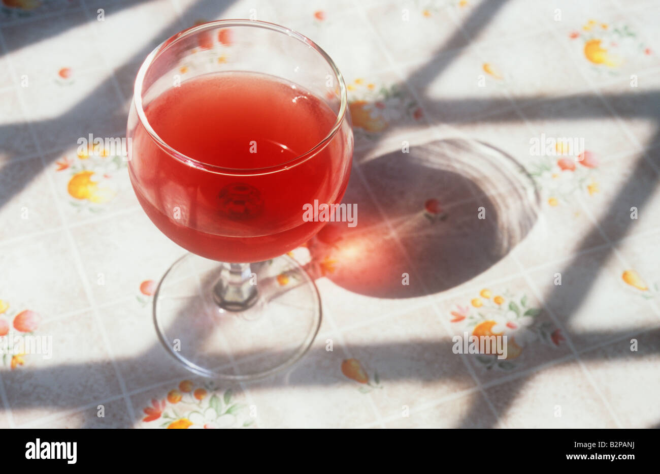 Weinglas mit roten Wein oder Fruchtsaft auf blumige Tischdecke und eigenen  Schatten zwischen den Schatten der Diamant verbleit Fenster Stockfotografie  - Alamy