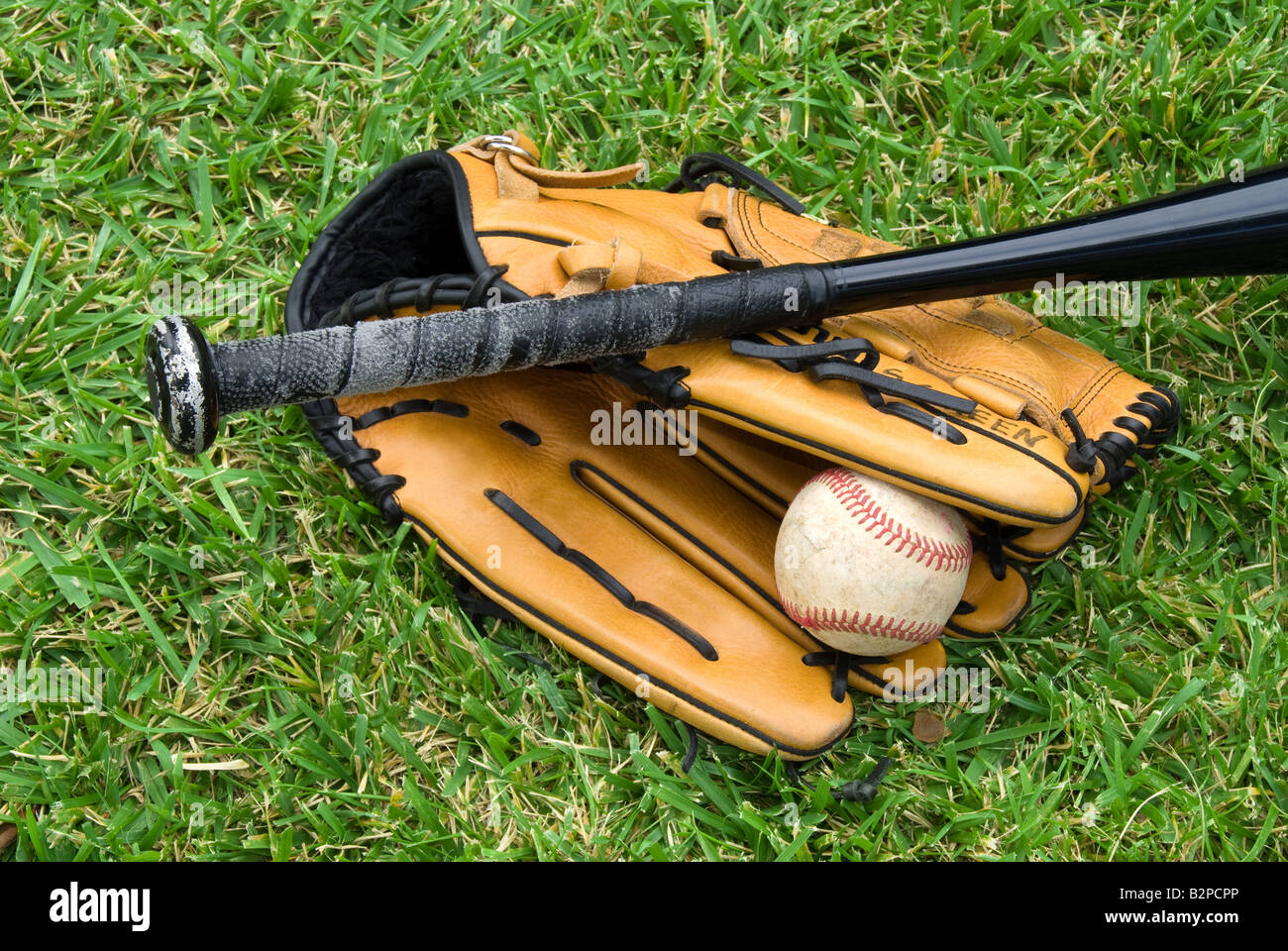 Ein Baseball-Handschuh-Ball und Schläger liegen in der Wiese vor einem Spiel Stockfoto