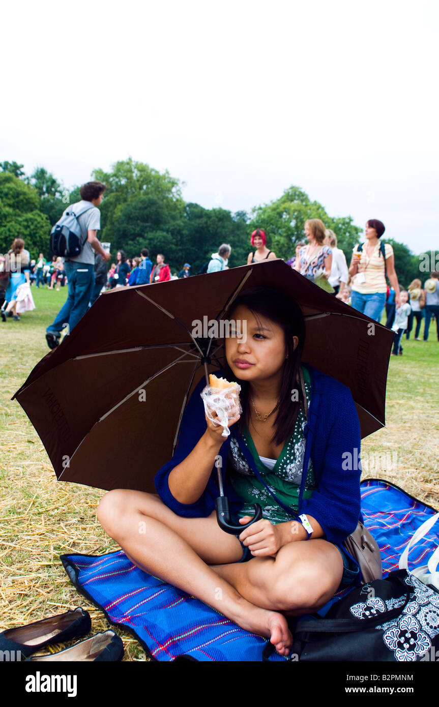 Mädchen sitzt unter einem Regenschirm, während des Essens ein Picknick auf einem nassen Sommerfestival in london Stockfoto