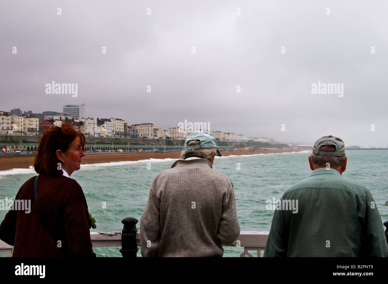 Drei Menschen stehen am Pier von Brighton in West Sussex an einem windigen Tag bewölkt. Stockfoto