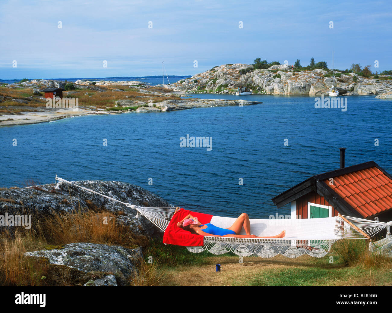 Frau in Hängematte auf Huvudskar Huvudskär Insel ruhen mit roten Sommerhaus in schwedischen Schären südlich von Stockholm Stockfoto
