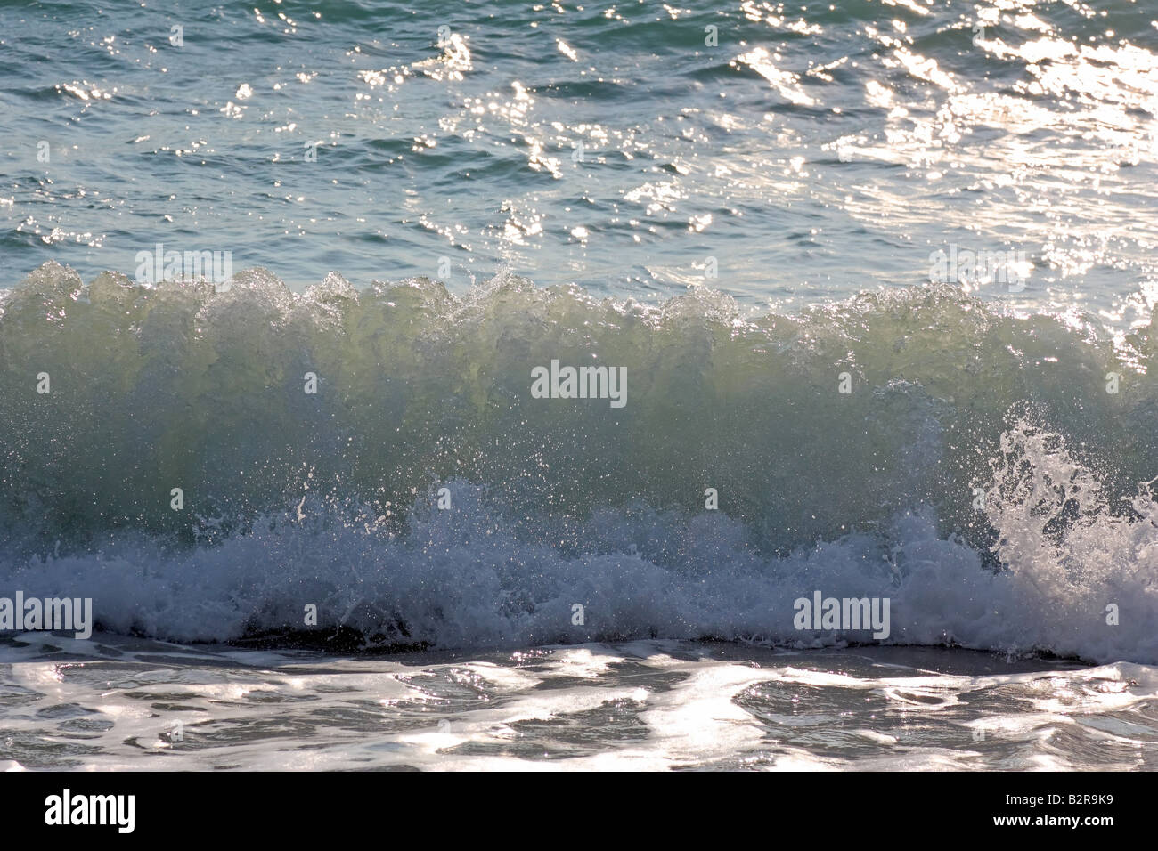Eine Hintergrundbeleuchtung Wellen am Ufer brechen Stockfoto