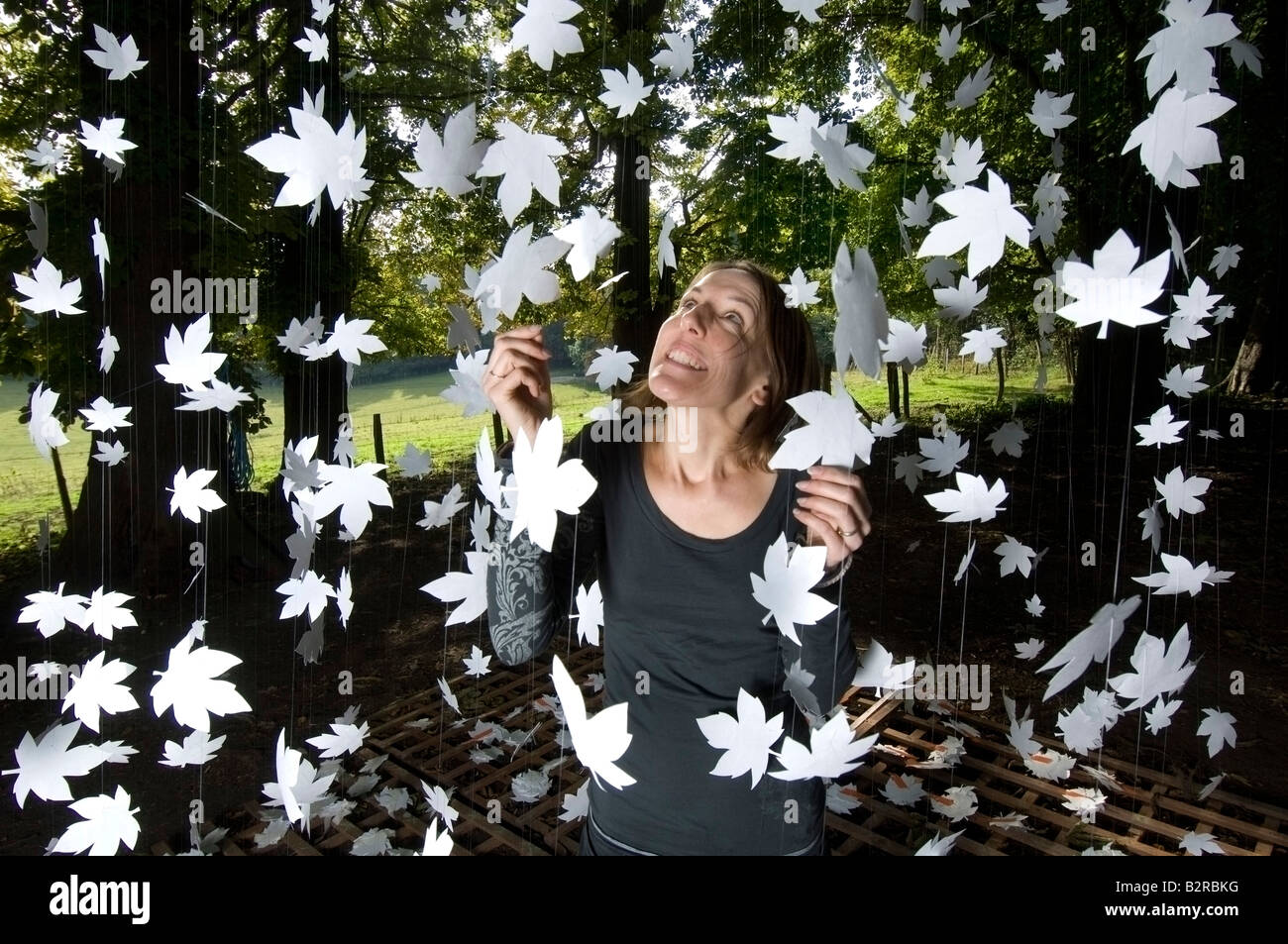 Eine Frau mit einem Vorhang aus Bergahorn Blattformen unter einem Cluster von altem Baumbestand im Rahmen einer Kunstausstellung im Freien ausgesetzt Stockfoto