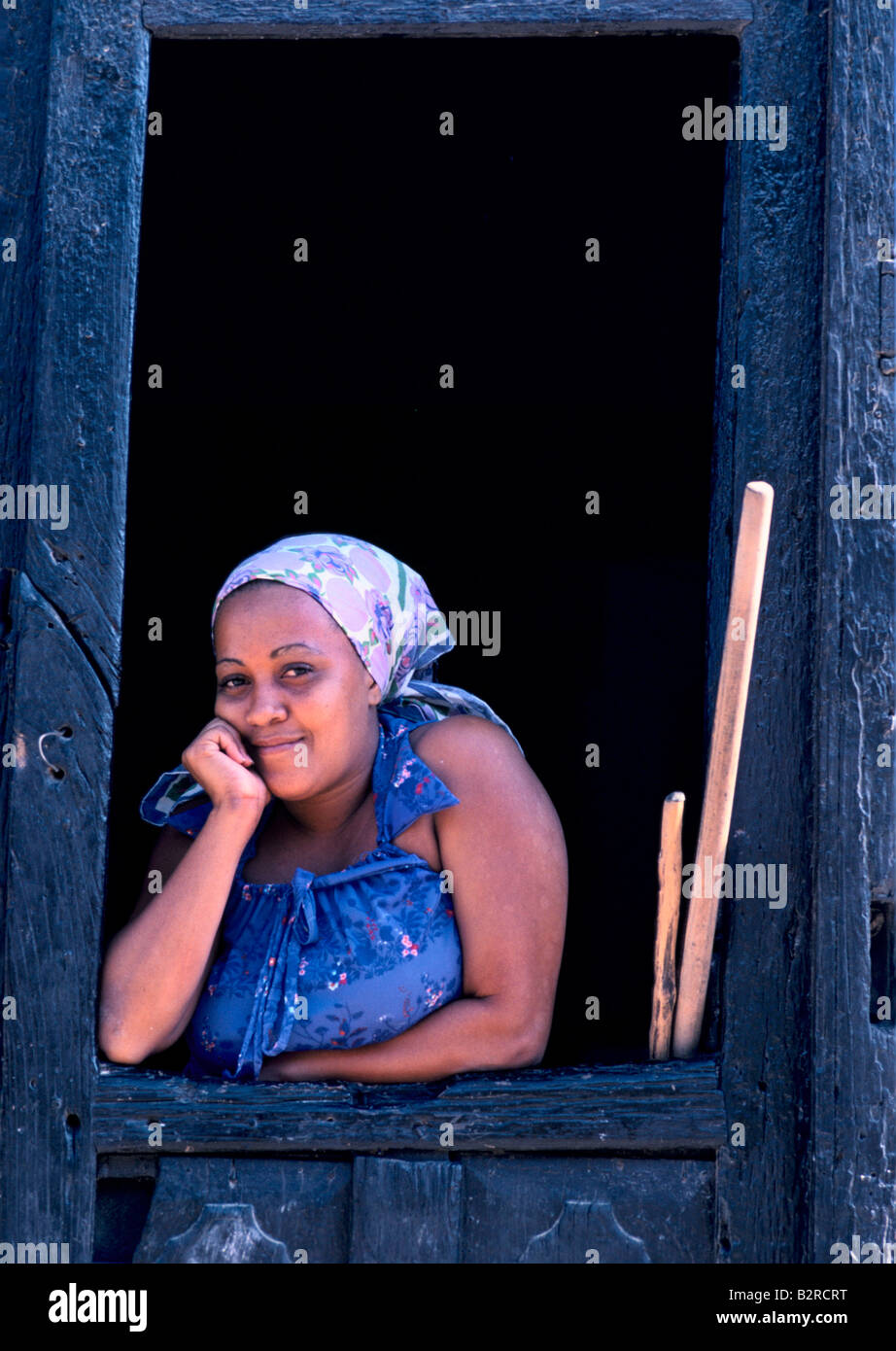 Junge kubanische Frau mit Kopftuch, Blick aus einem Holzrahmen in einer Tür lächelnd zu Kamera in Trinidad, Kuba Stockfoto