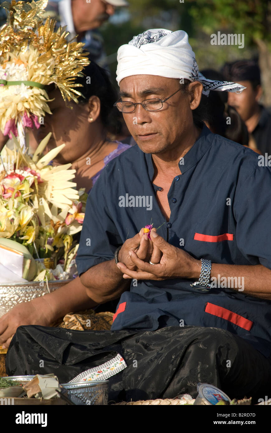 Bali Indonesien Kuta Strand Mann beten Feuerbestattung Zeremonie hindu religiösen Menschen sammeln Blumen Weihrauch brennen mit display Stockfoto