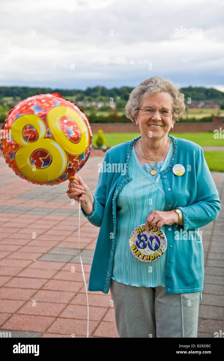 EINE ÄLTERE FRAU HOLDING BALOON AN IHREM 80. GEBURTSTAG Stockfoto