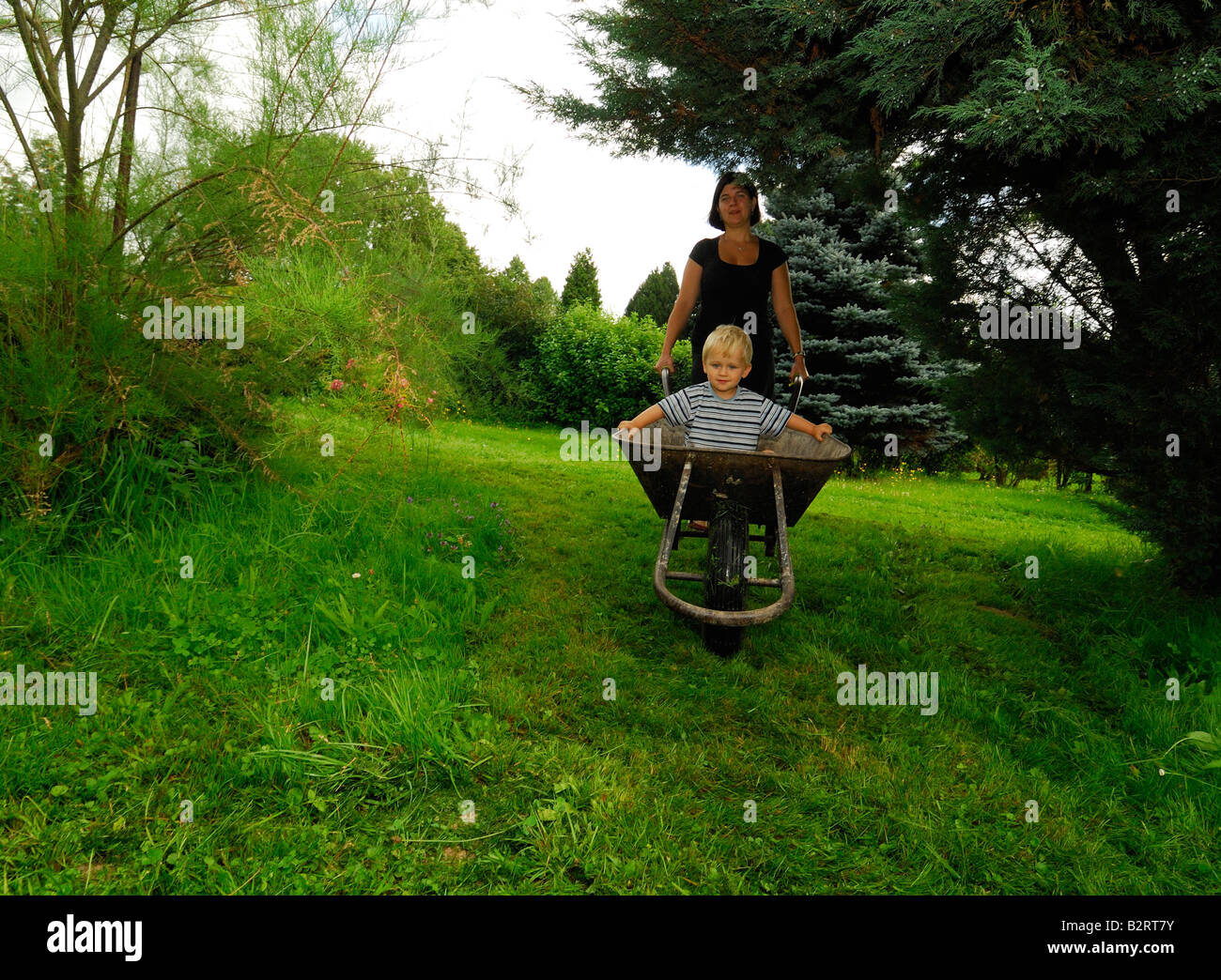 Mutter ihren Sohn in eine Schubkarre Hand durch den Garten bewegen Stockfoto