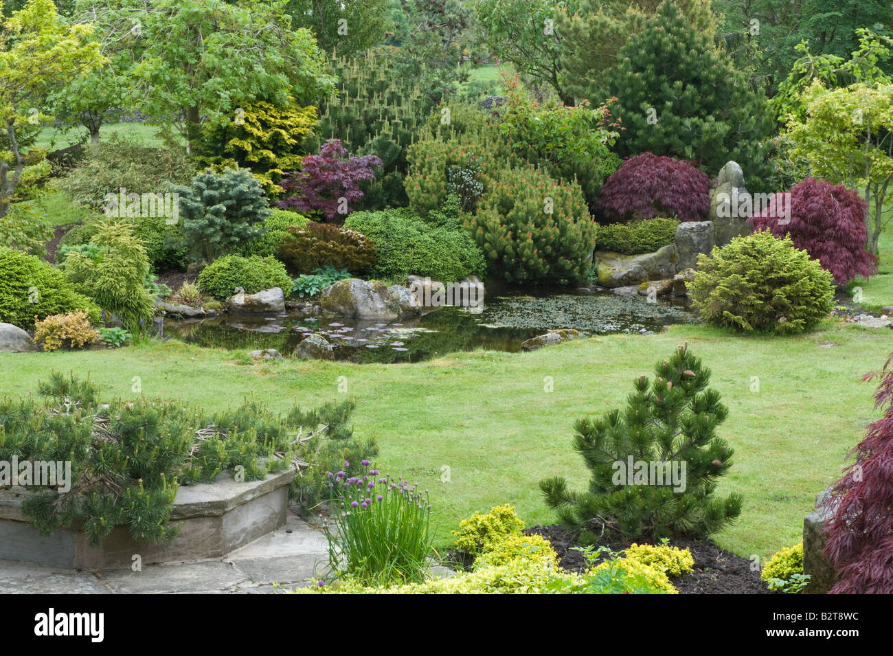 Designed by Bahaa Seedhom mit Terrasse und Teich mit lokalem Sand-Stein, Sträucher, Bäume, North Yorkshire England Mai Steingarten Stockfoto