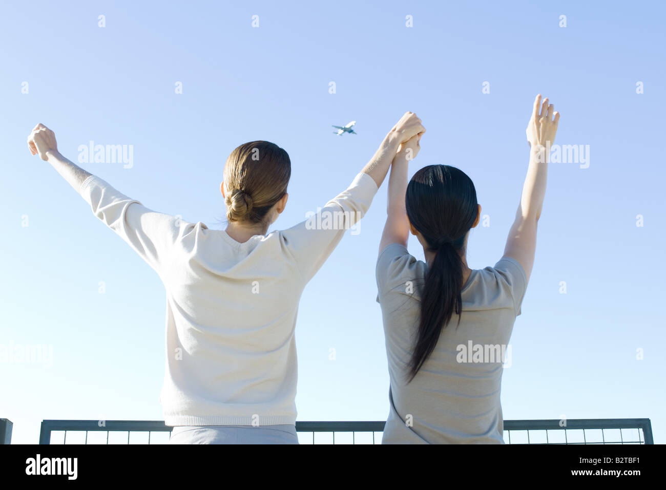 Zwei Frauen, die am Flugzeug im Himmel, Hand in Hand, Arme heben, Rückansicht Stockfoto
