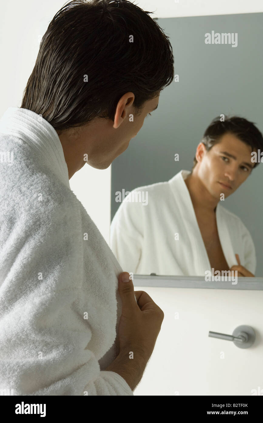 Man betrachtet sich im Spiegel, zieht seinen Bademantel geöffnet Stockfoto