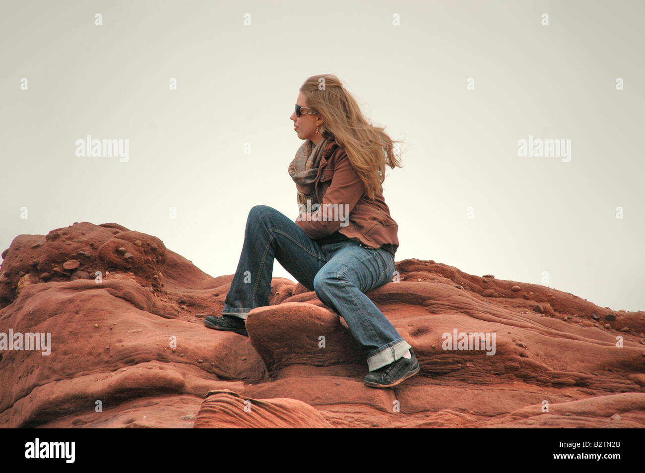 eine junge Frau sitzt auf einem Küstenfelsen, Blick auf das Meer. Stockfoto