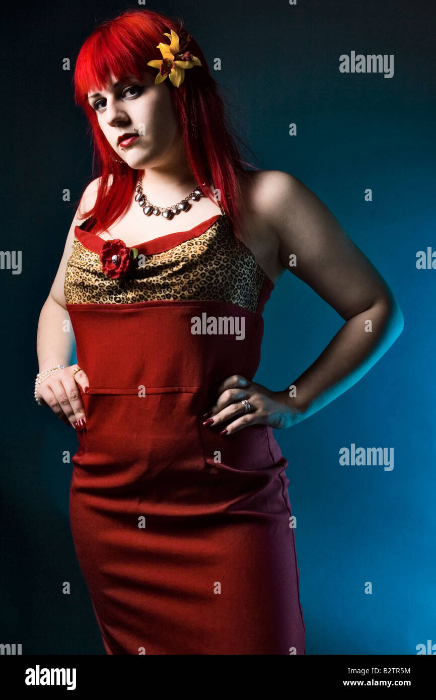 Mode Porträt eines jungen Mädchens der Goth mit leuchtend roten Haaren in einem roten Kleid auf einem blauen Hintergrund. Stockfoto