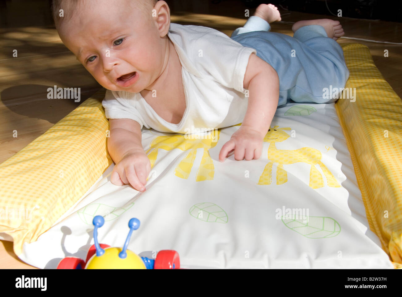 Baby Boy auf Änderung in Frustration für Toy Spider Matte Weinen auf Bauch liegend Stockfoto