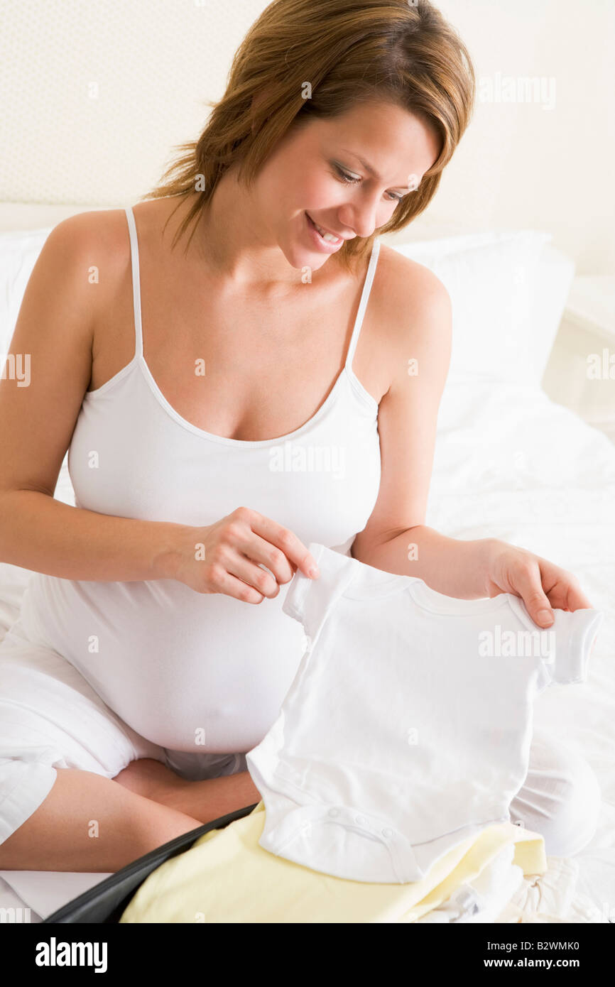 Schwangere Frau Verpackung Baby Kleidung im Koffer lächelnd Stockfoto