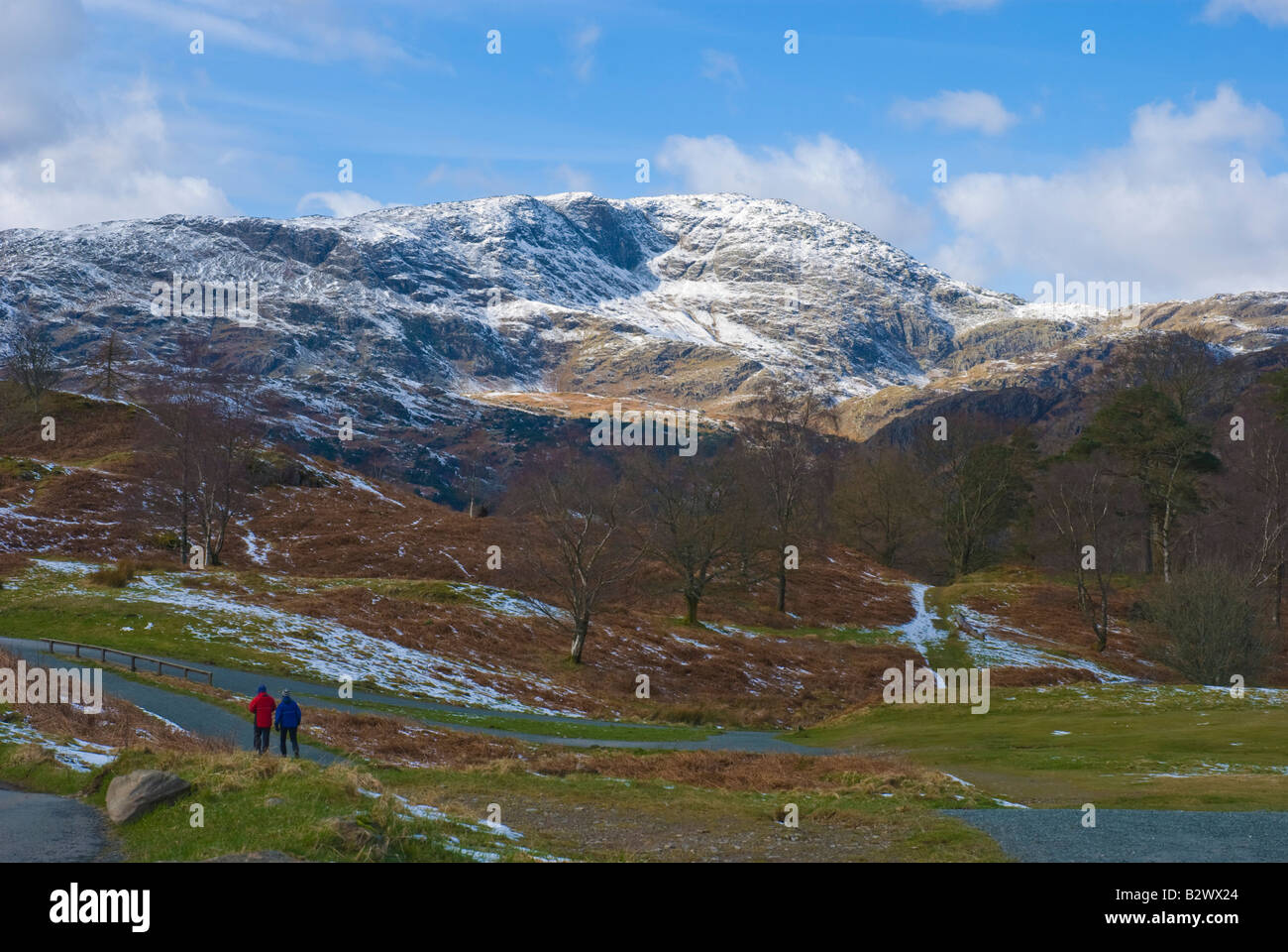 Wanderer auf Pfad um Tarn Hows mit Schnee bedeckt Wetherlam im Hintergrund Stockfoto