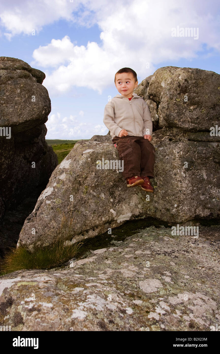 Frecher kleiner Junge mit lustigen Ausdruck sitzen auf Granit Tor im Dartmoor National Park Stockfoto