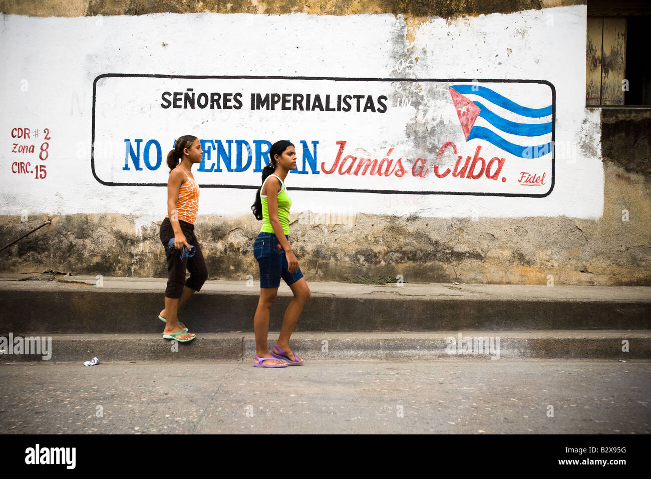 Zwei Mädchen im Teenageralter Fuß durch eine Wandmalerei in Spanisch Imperialisten geehrte Damen und Herren sagen, erhalten Sie nie in Baracoa Kuba Kuba auf Donner Stockfoto