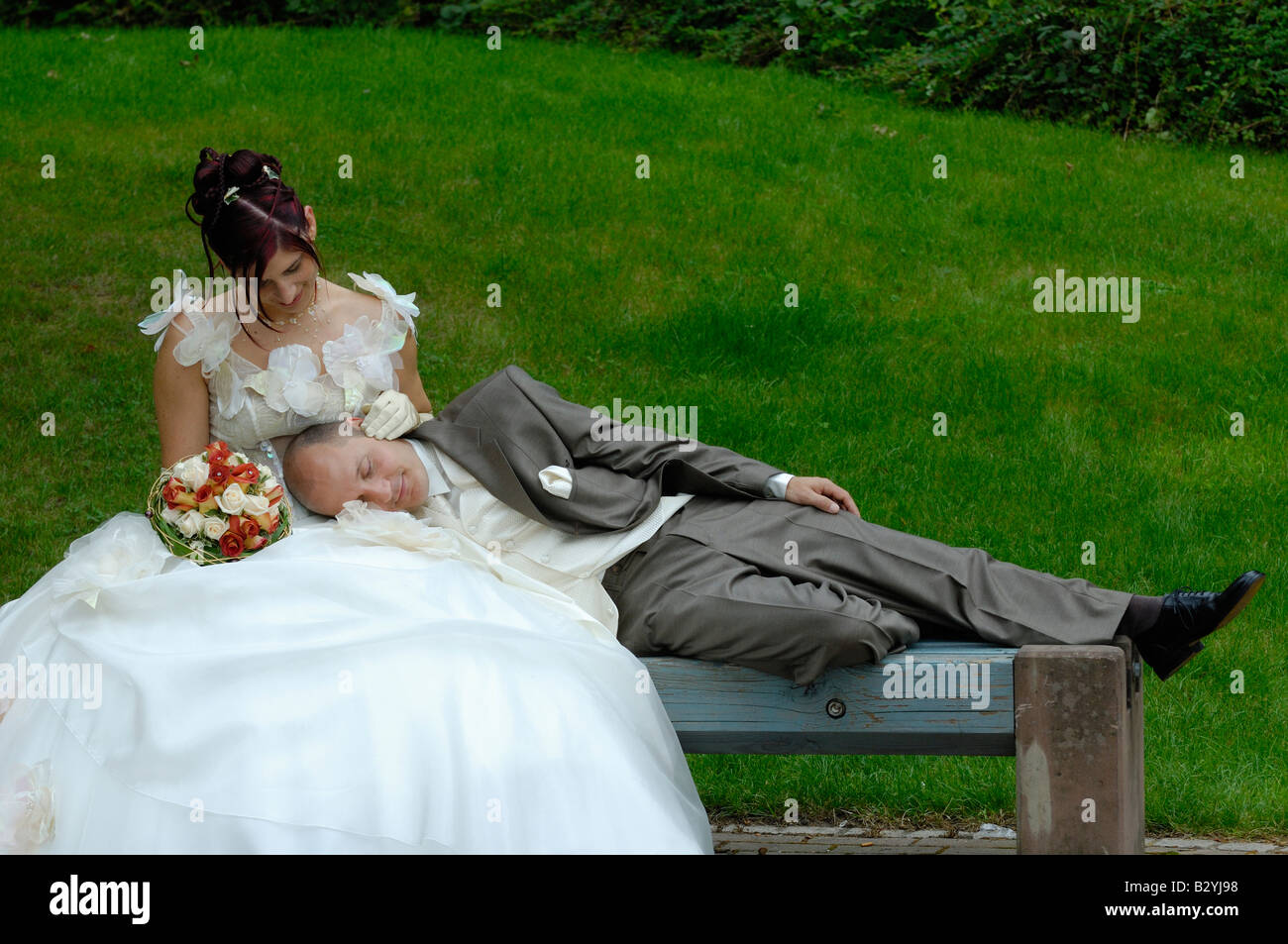 Brautpaar mit Mann schlafend auf seiner Frau in der Bank Park, Frankreich Stockfoto