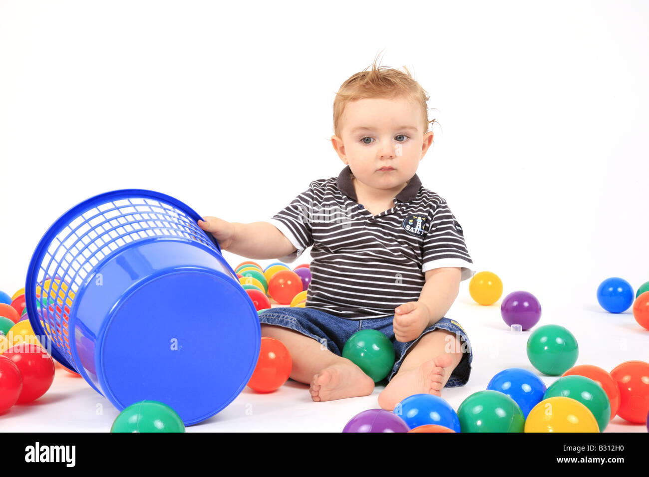 Kleiner Junge sitzt zwischen den farbigen Kugeln Stockfoto