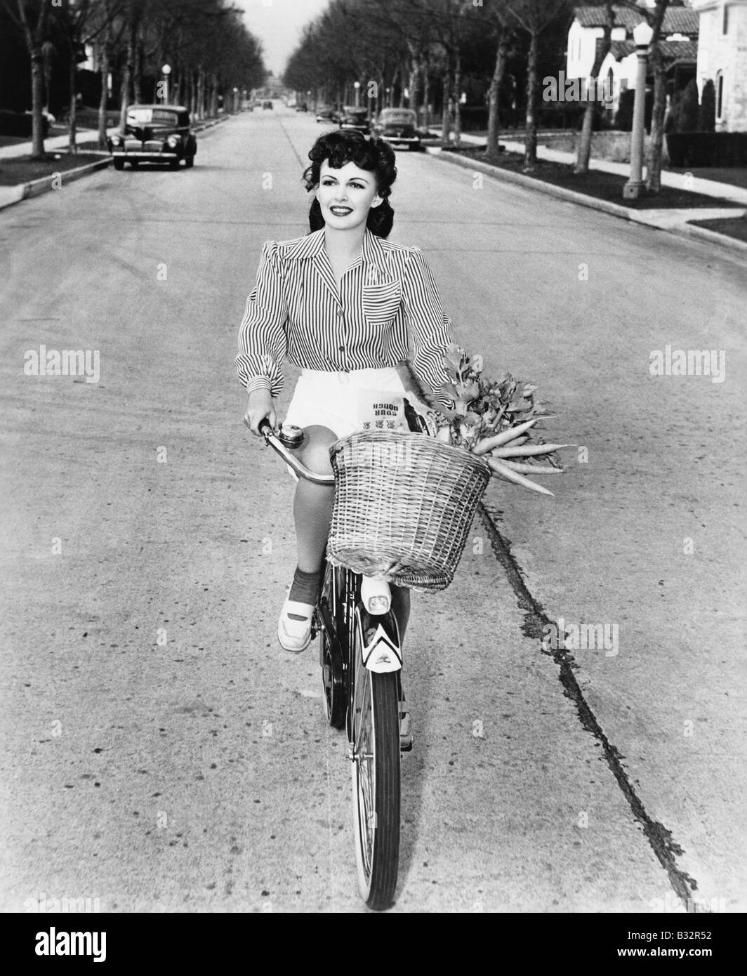 Junge Frau mit ihrem Fahrrad mit Korb voller Blumen und Karotten Stockfoto