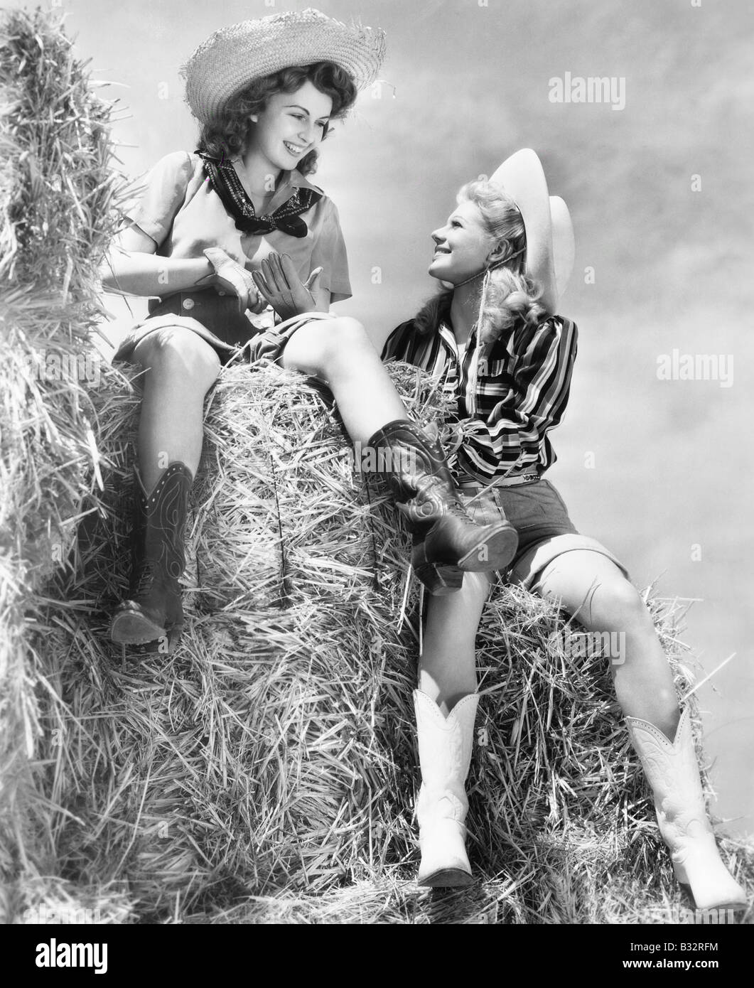 Zwei Frauen sitzen auf einem Heuhaufen Cowboy-Hüte Stockfoto