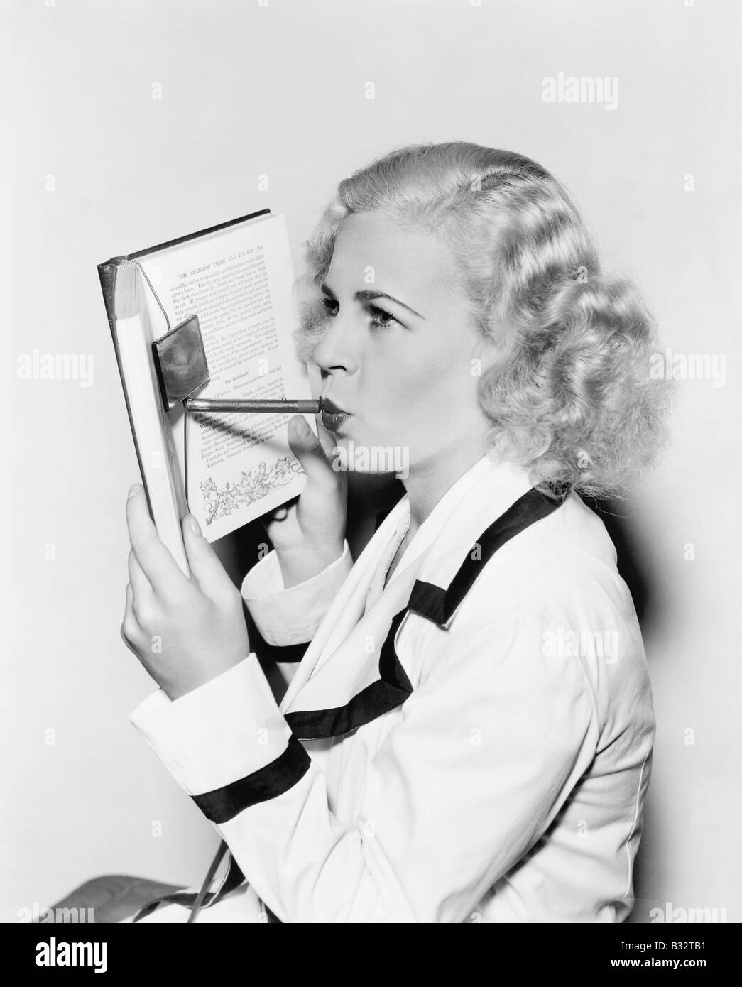 Junge Frau verbirgt ihr Gesicht hinter einem Buch Auftragen von Lippenstift Stockfoto