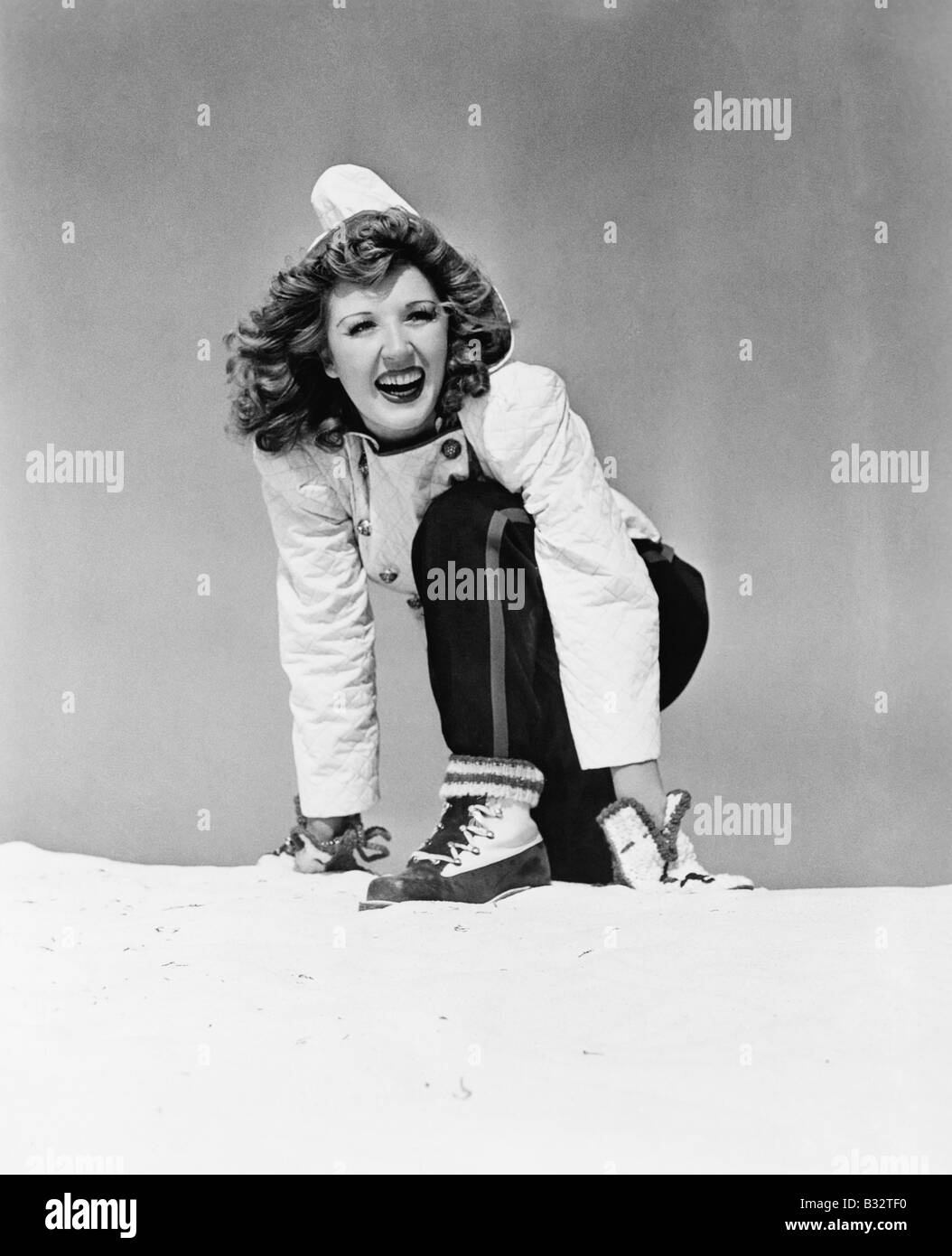 Junge Frau im Schnee kniend und lächelnd Stockfoto