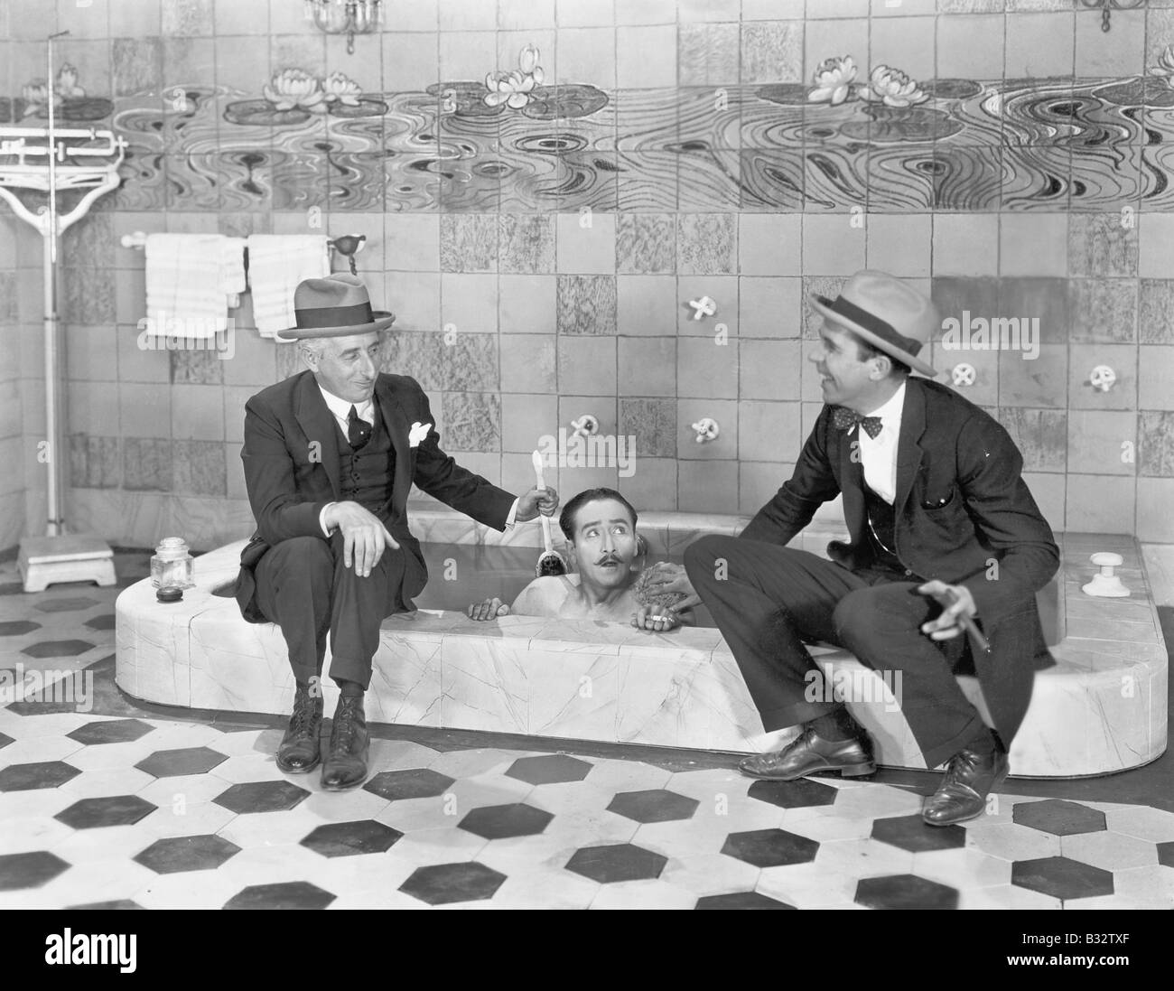Zwei Männer sitzen am Rand der Badewanne in Anzügen und schrubben eine Freunde zurück Stockfoto