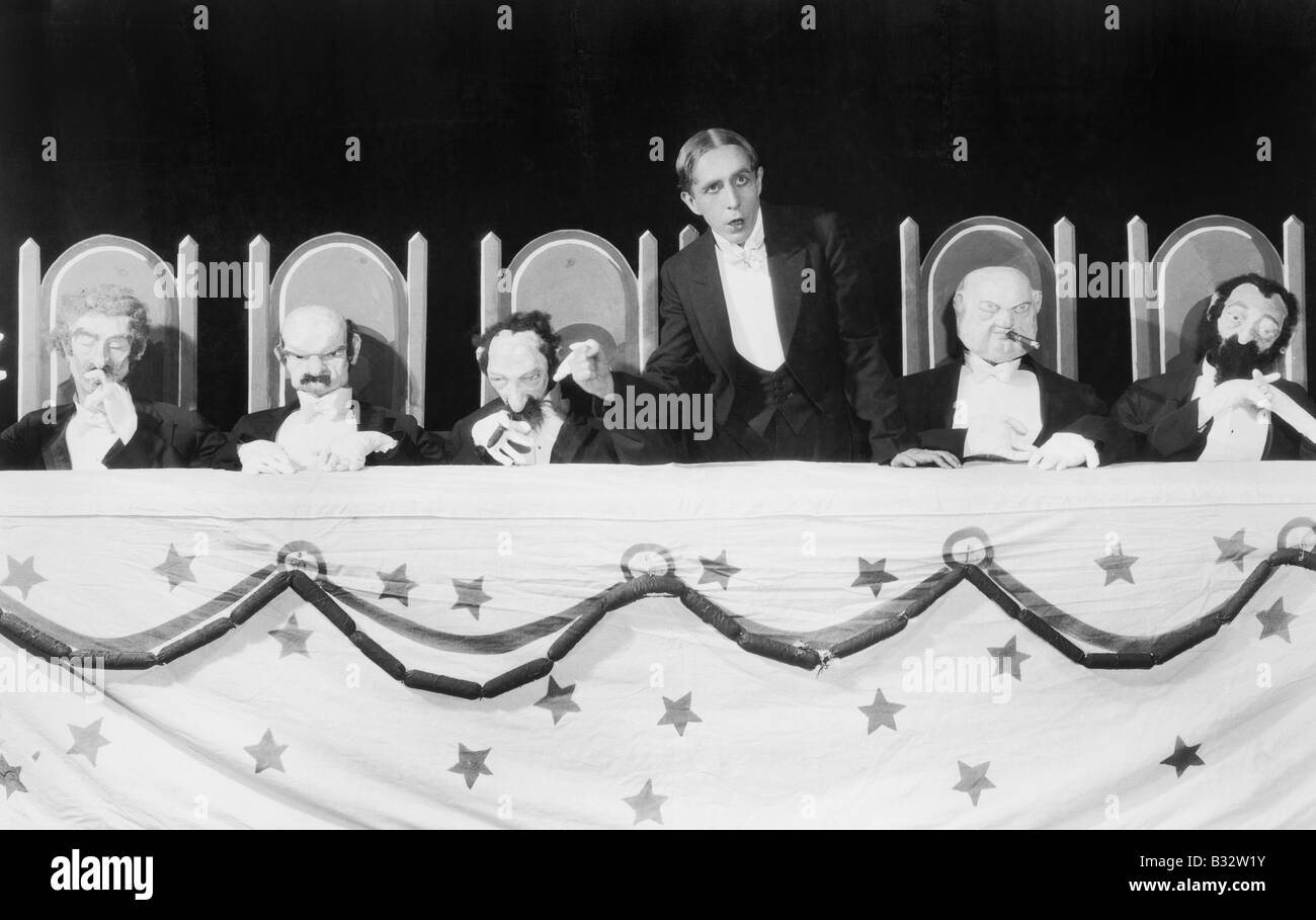 Mann hält eine Rede mit fünf Charakter-Puppen, die am Tisch sitzen Stockfoto