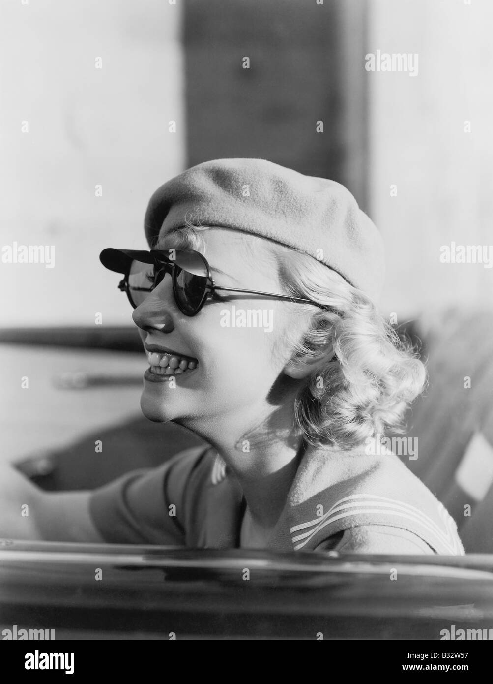 Junge Frau mit Baskenmütze Sonnenbrille im Auto unterwegs Stockfoto